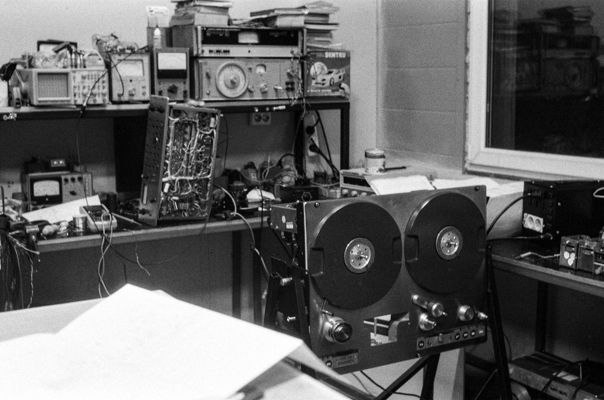 Black and white photo of vintage audio repair shop with magnetic tape equipment and electronics.