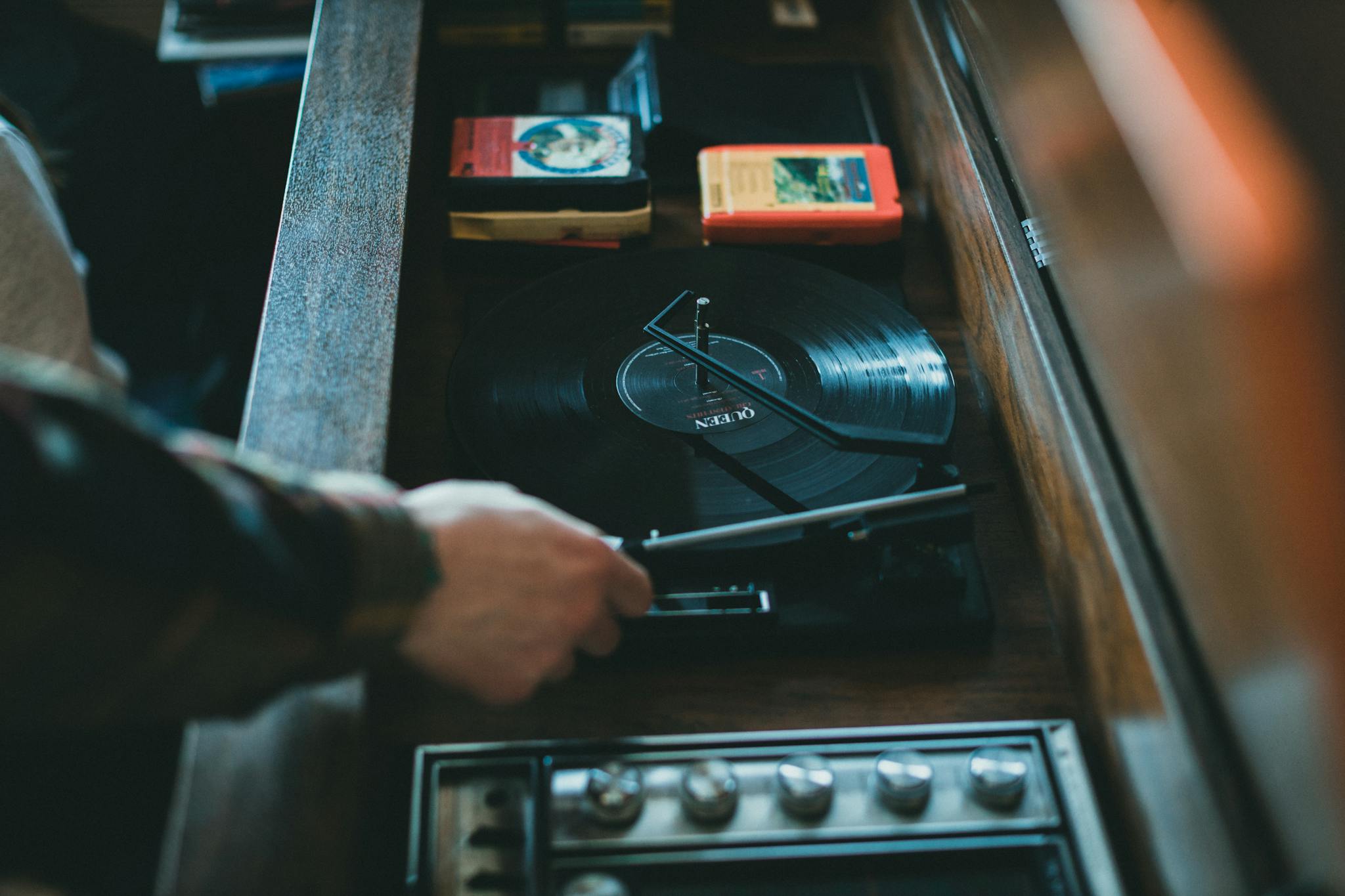 Close-up of a vintage turntable playing a vinyl record with visible hand adjusting. Classic music setup indoors.
